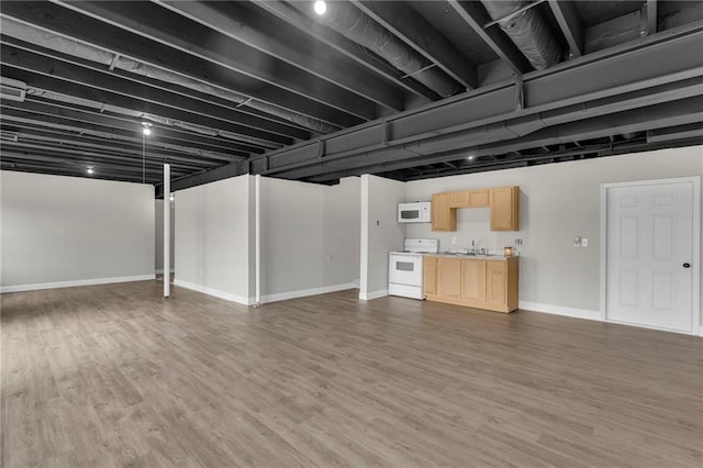 finished below grade area featuring a sink, baseboards, and wood finished floors