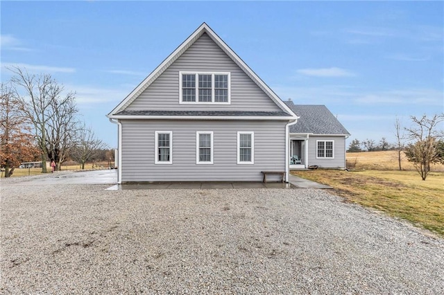 rear view of house with gravel driveway and a shingled roof