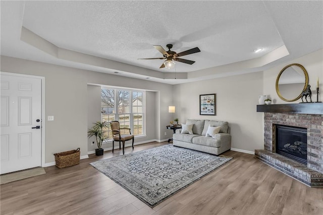 living area with a fireplace, a raised ceiling, a textured ceiling, wood finished floors, and baseboards