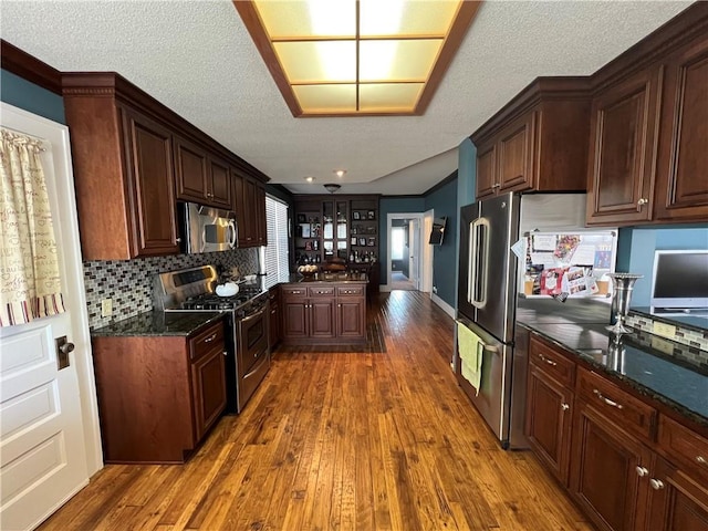 kitchen featuring a textured ceiling, appliances with stainless steel finishes, decorative backsplash, and wood finished floors