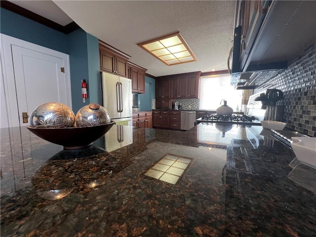 kitchen featuring a textured ceiling, appliances with stainless steel finishes, dark stone countertops, and tasteful backsplash