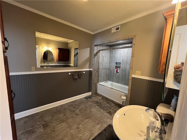 full bath featuring visible vents, bath / shower combo with glass door, wainscoting, crown molding, and a sink