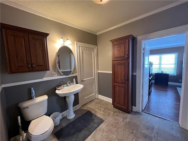 bathroom featuring a wainscoted wall, ornamental molding, a textured ceiling, and toilet