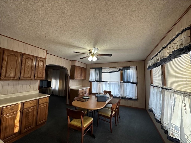 kitchen with arched walkways, brown cabinetry, light countertops, and dark colored carpet