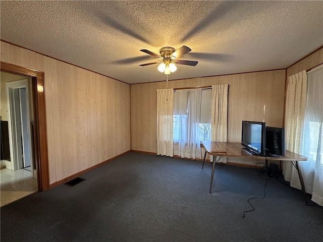 unfurnished office featuring carpet, visible vents, a ceiling fan, a textured ceiling, and wooden walls