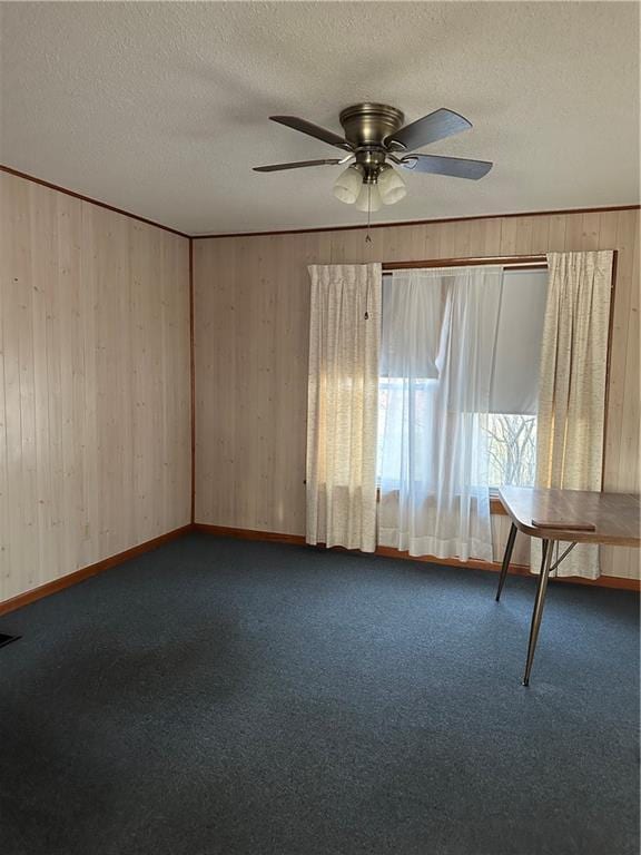 carpeted spare room with a ceiling fan, baseboards, wooden walls, and a textured ceiling