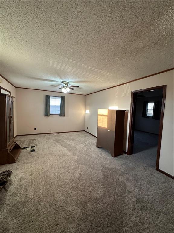 unfurnished bedroom featuring carpet, crown molding, a ceiling fan, a textured ceiling, and baseboards