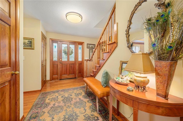 foyer entrance with stairs, baseboards, light wood finished floors, and a textured ceiling