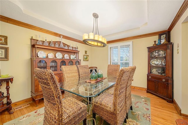 dining space featuring visible vents, baseboards, a tray ceiling, and light wood-style floors