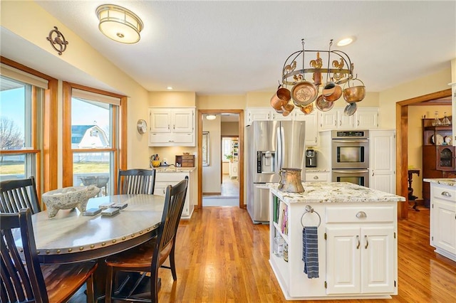 kitchen featuring light stone countertops, light wood finished floors, a kitchen island, appliances with stainless steel finishes, and white cabinetry