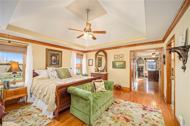 bedroom with crown molding, baseboards, light wood-type flooring, and a tray ceiling