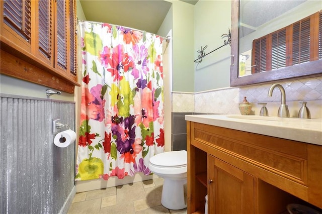 full bath featuring toilet, a shower with shower curtain, vanity, wainscoting, and tile walls