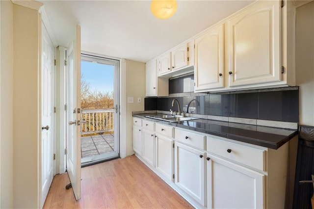 kitchen with a sink, light wood-type flooring, backsplash, and white cabinets