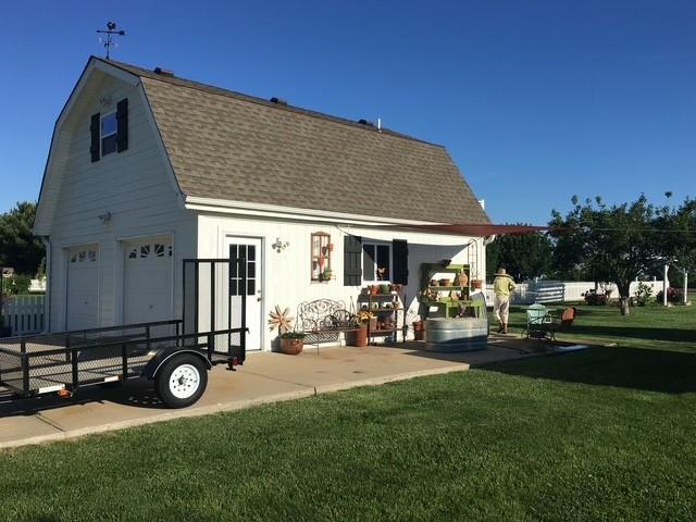 back of house featuring a yard, a gambrel roof, a garage, and roof with shingles