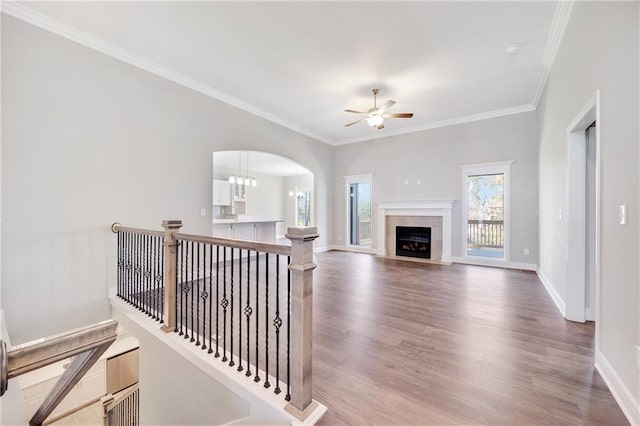 living room featuring hardwood / wood-style flooring, a tile fireplace, crown molding, and ceiling fan with notable chandelier