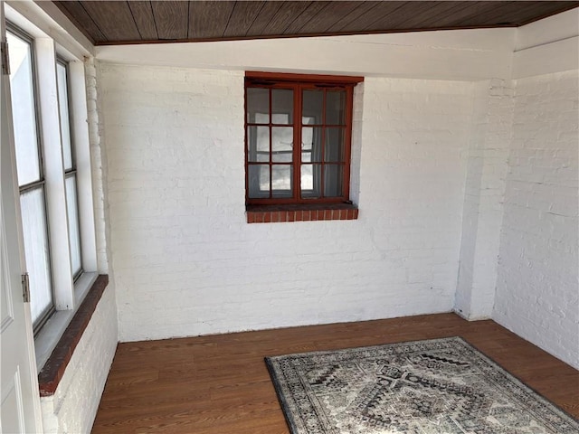 spare room featuring brick wall, dark wood-type flooring, and wood ceiling