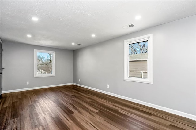 empty room with a textured ceiling, dark wood-type flooring, recessed lighting, and baseboards