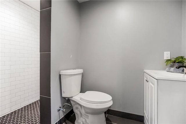 bathroom featuring toilet, baseboards, tiled shower, and vanity