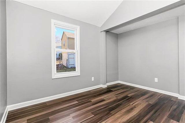 spare room featuring dark wood-style floors, lofted ceiling, and baseboards