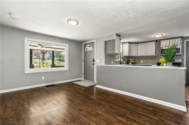 kitchen with a sink, light countertops, gray cabinets, tasteful backsplash, and dark wood finished floors