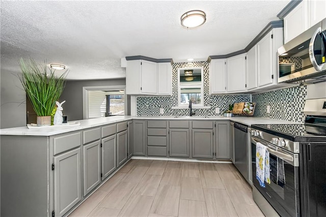 kitchen with gray cabinets, light countertops, appliances with stainless steel finishes, a sink, and a peninsula