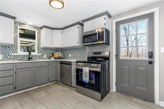 kitchen featuring stainless steel appliances, tasteful backsplash, gray cabinets, light countertops, and a sink