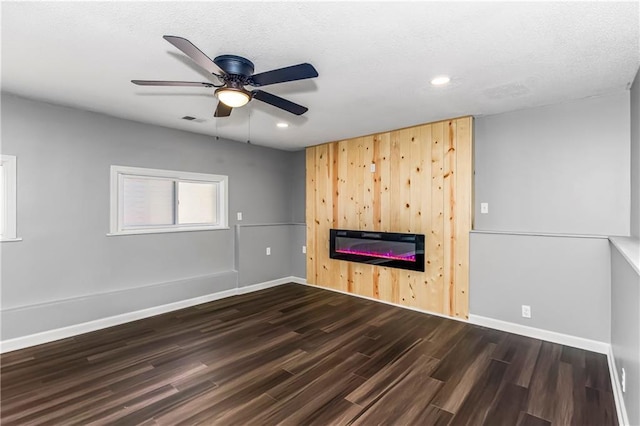 unfurnished living room featuring dark wood-type flooring, a glass covered fireplace, visible vents, and baseboards