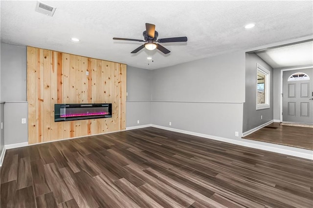 unfurnished living room with a textured ceiling, dark wood-style flooring, a glass covered fireplace, and visible vents