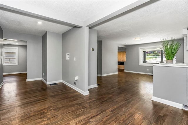 empty room with a textured ceiling, dark wood finished floors, visible vents, and baseboards