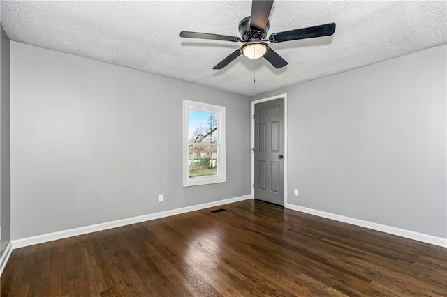 spare room with a textured ceiling, dark wood-type flooring, visible vents, and baseboards