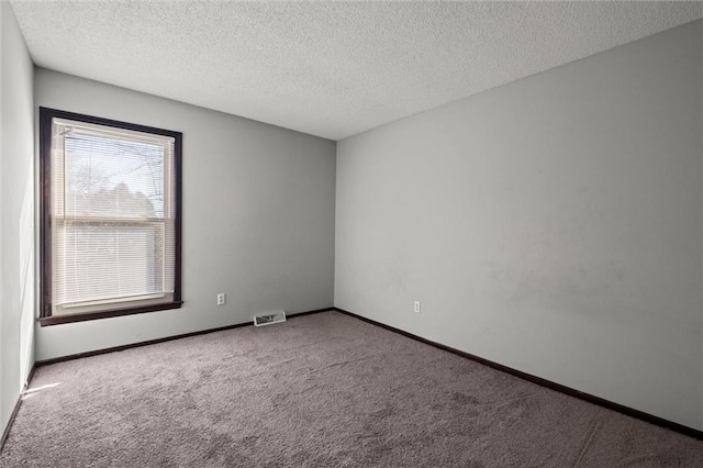 unfurnished room with a textured ceiling, carpet flooring, visible vents, and baseboards