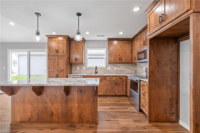 607 W Dryden St, Odessa, MO 64076 - kitchen with light wood-style flooring, brown cabinets, appliances with stainless steel finishes, and a kitchen island