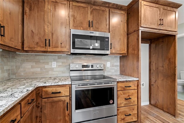 607 W Dryden St, Odessa, MO 64076 - kitchen with stainless steel appliances, light wood-style flooring, brown cabinetry, and decorative backsplash