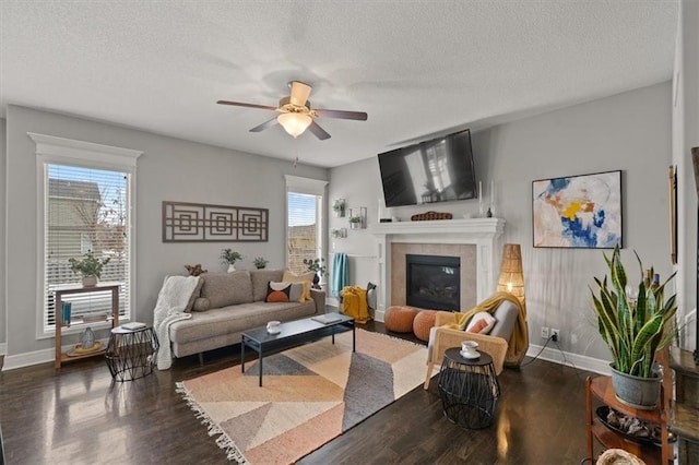 living room with a textured ceiling, a tile fireplace, dark wood finished floors, and a ceiling fan