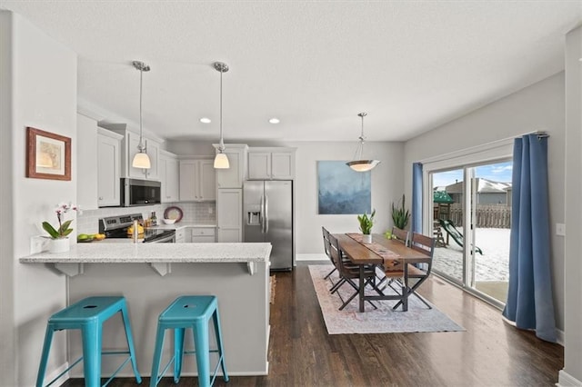 kitchen featuring a breakfast bar, decorative light fixtures, tasteful backsplash, appliances with stainless steel finishes, and a peninsula