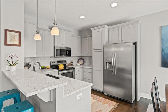 kitchen with decorative backsplash, appliances with stainless steel finishes, a breakfast bar, decorative light fixtures, and a peninsula