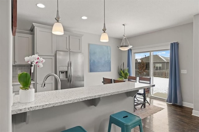 kitchen with light stone countertops, stainless steel fridge, a breakfast bar area, and pendant lighting