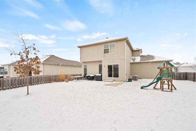 snow covered house featuring cooling unit, a playground, and fence