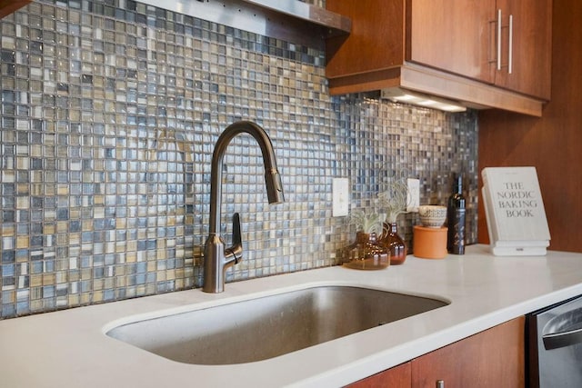 kitchen featuring brown cabinetry, a sink, light countertops, stainless steel dishwasher, and backsplash