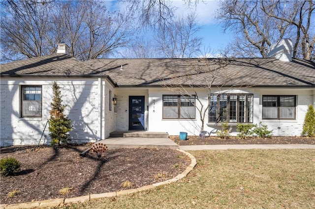 ranch-style house featuring brick siding, a chimney, a front lawn, and a shingled roof