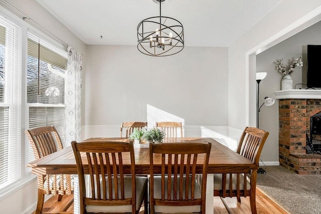 dining space featuring wood finished floors, a brick fireplace, baseboards, and an inviting chandelier