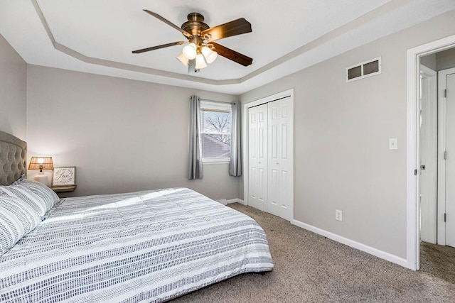 bedroom with a tray ceiling, baseboards, visible vents, and carpet flooring