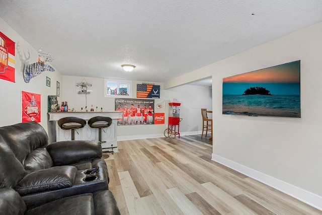 living room featuring light wood finished floors, a dry bar, a textured ceiling, and baseboards