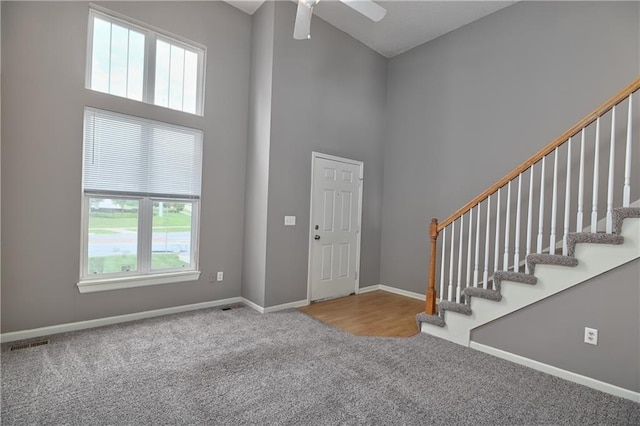 foyer entrance with carpet, visible vents, a towering ceiling, baseboards, and stairs