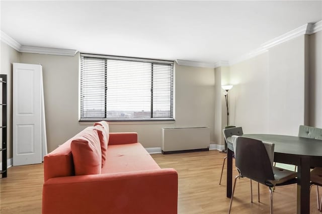 living area with crown molding, light wood-style flooring, and baseboards