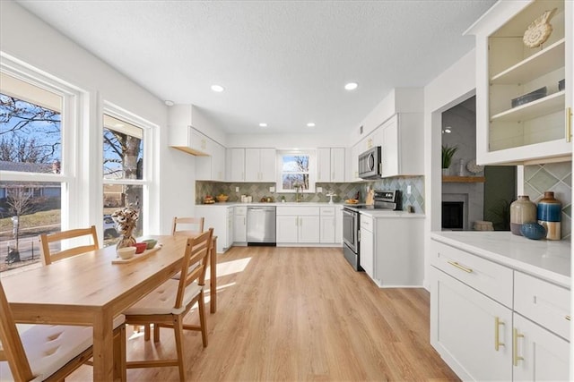 kitchen with light countertops, backsplash, light wood-style flooring, appliances with stainless steel finishes, and white cabinets