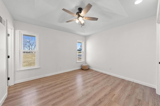 empty room featuring light wood finished floors, recessed lighting, a raised ceiling, ceiling fan, and baseboards