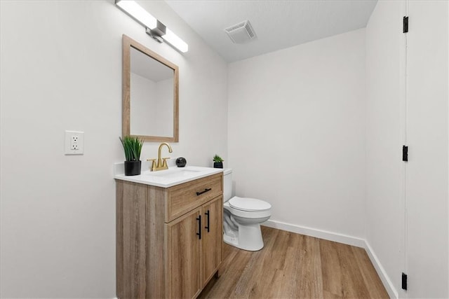 half bathroom featuring toilet, wood finished floors, vanity, visible vents, and baseboards