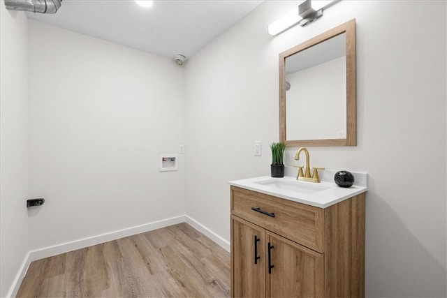 clothes washing area featuring hookup for a washing machine, laundry area, a sink, baseboards, and light wood-style floors