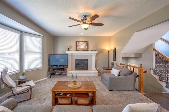 living area featuring baseboards, carpet, a tile fireplace, a textured ceiling, and a ceiling fan